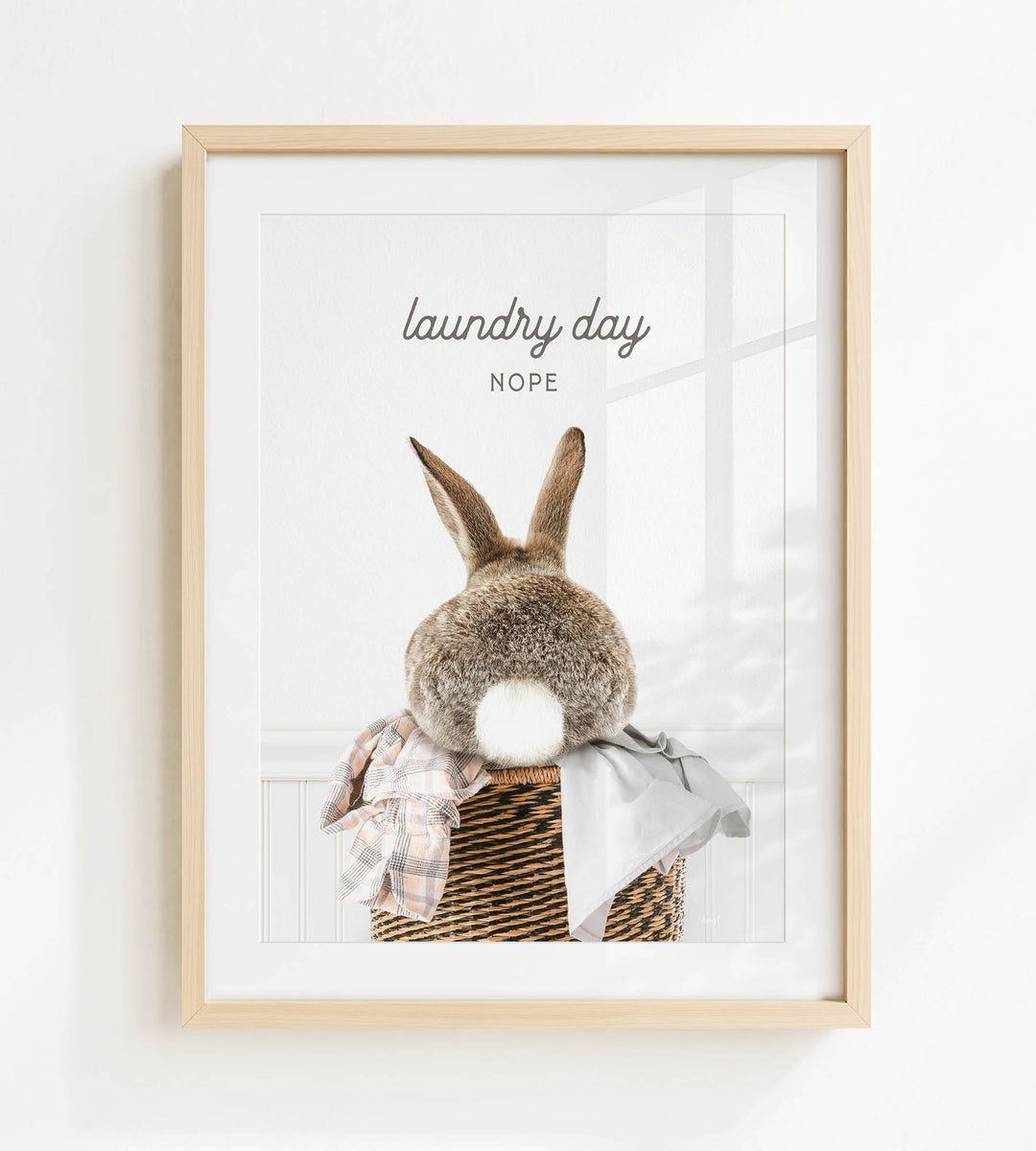 A framed image of a rabbit sitting in a basket filled with laundry, with the text "laundry day NOPE" displayed above the rabbit.