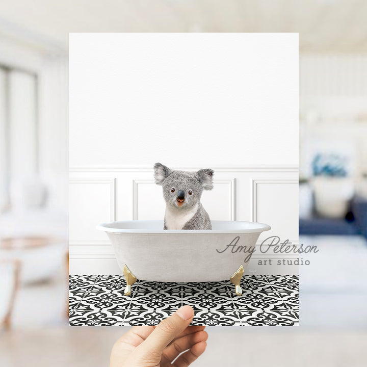 a hand holding a photo of a koala in a bathtub