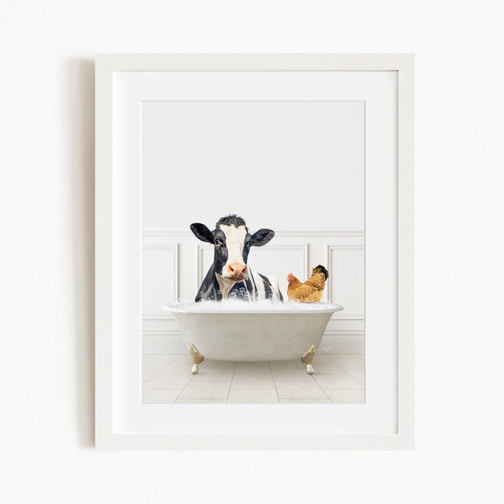 A black and white cow is sitting in a white bathtub, with a chicken standing nearby, in a white-framed picture.