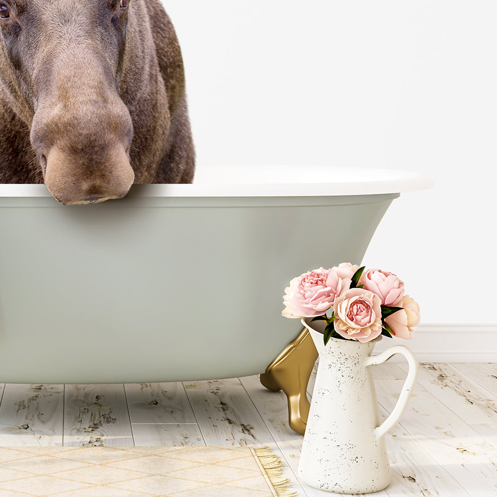 A brown moose is standing in a green bathtub, with a white vase of pink flowers placed next to it on a white wooden floor.