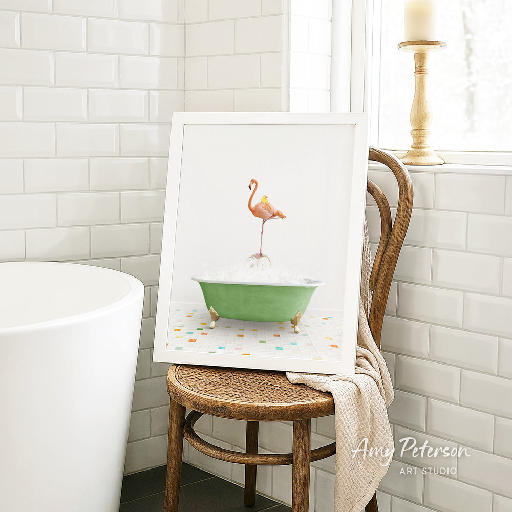 A framed image of a pink flamingo standing in a green bathtub is displayed on a wooden chair in a bathroom setting.