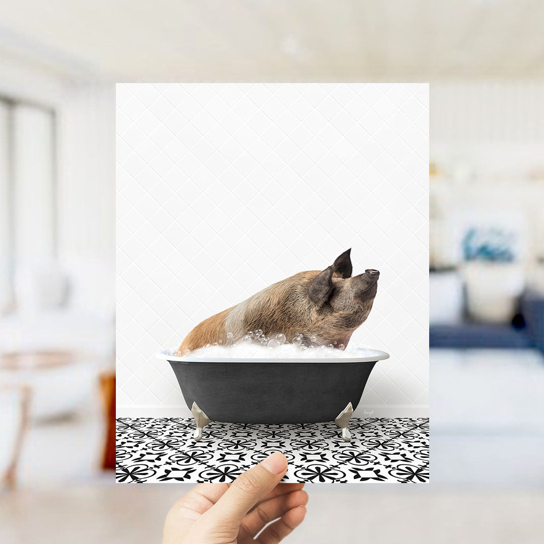 A hand holds up a framed image of a pig sitting in a bathtub filled with bubbles, with a black and white patterned floor in the background.