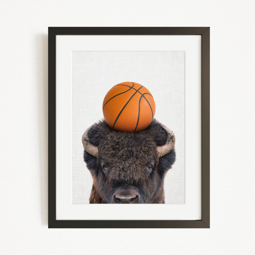 A framed image of a buffalo with a basketball resting on its head.