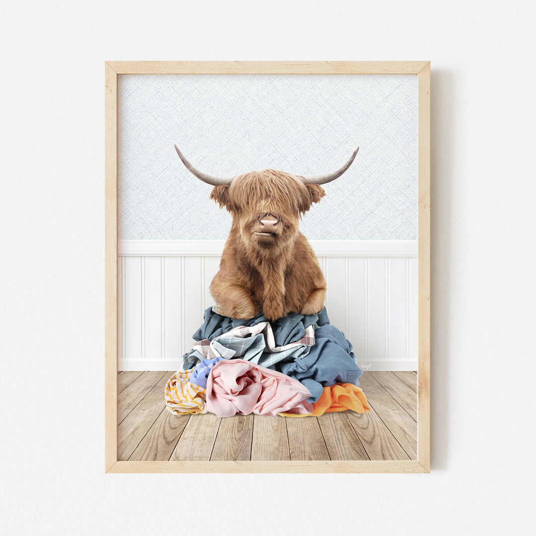 a framed photograph of a highland cow sitting on a pile of clothes