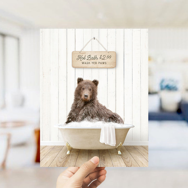 A brown bear sitting in a bathtub filled with water, with a sign above the bear that reads "Hot Bath $2.00 WASH YOUR Paws".