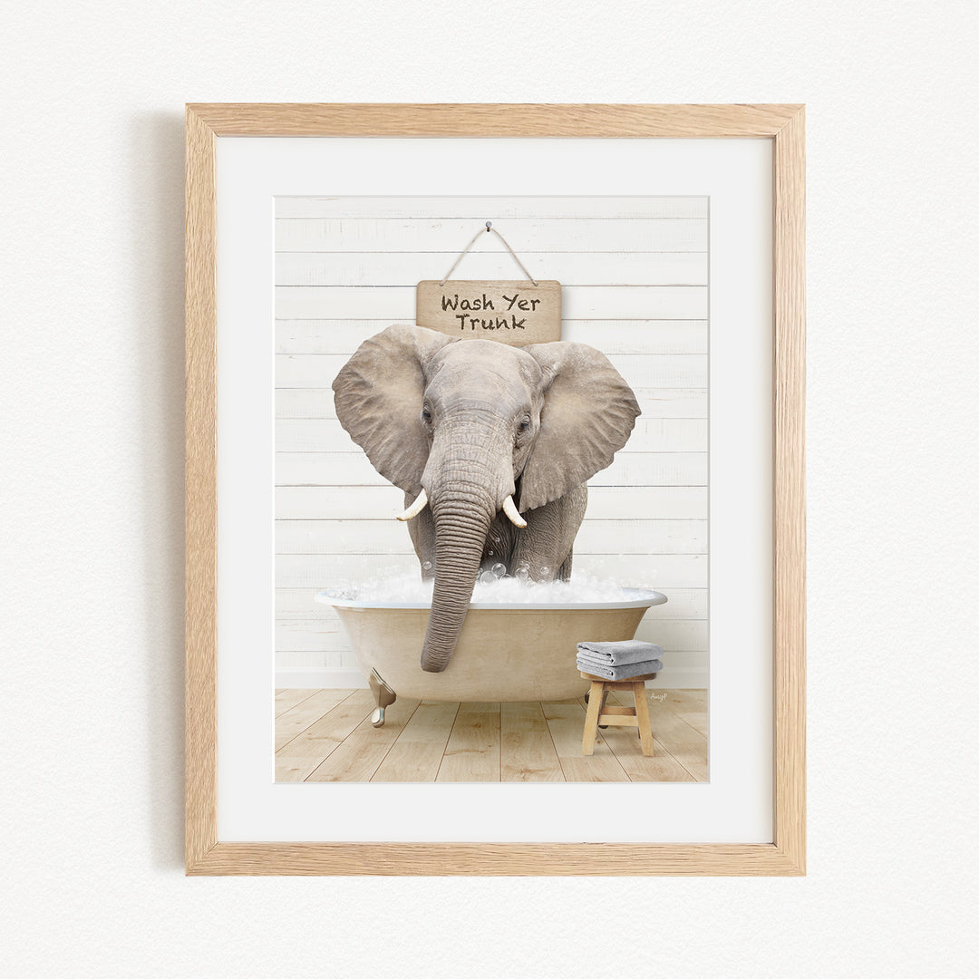 A framed image of an elephant standing in a bathtub, with a sign above it that says "Wash Yer Trunk".