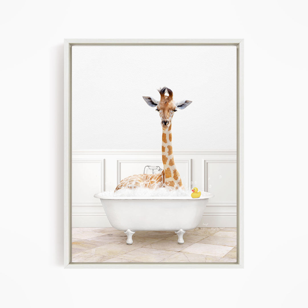 A giraffe sitting in a white bathtub filled with bubbles, with a yellow rubber duck floating in the water.