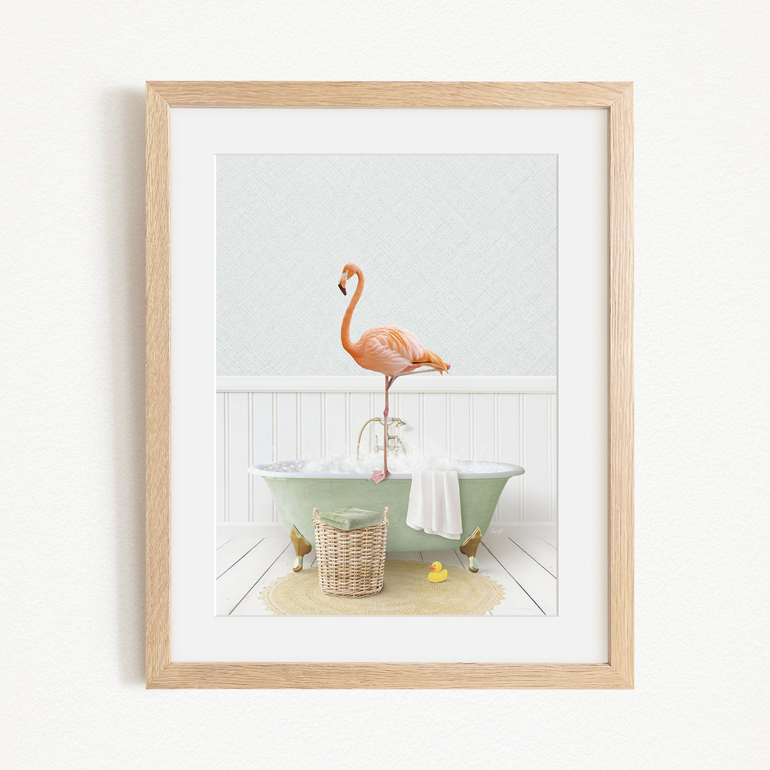 A framed image depicting a pink flamingo standing on the edge of a green bathtub filled with water, with a basket of bath toys and a yellow rubber duck nearby.