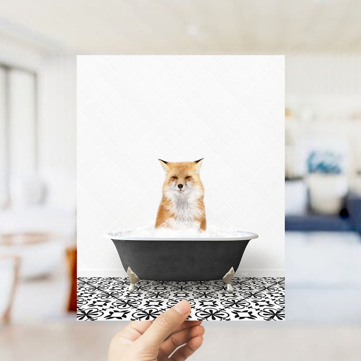 A hand holds up a framed image of a fox sitting in a bathtub filled with water, surrounded by a black and white patterned floor.