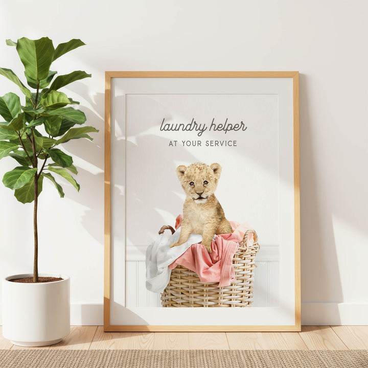 A framed poster with a photograph of a young lion cub sitting in a laundry basket, accompanied by the text "laundry helper at your service".