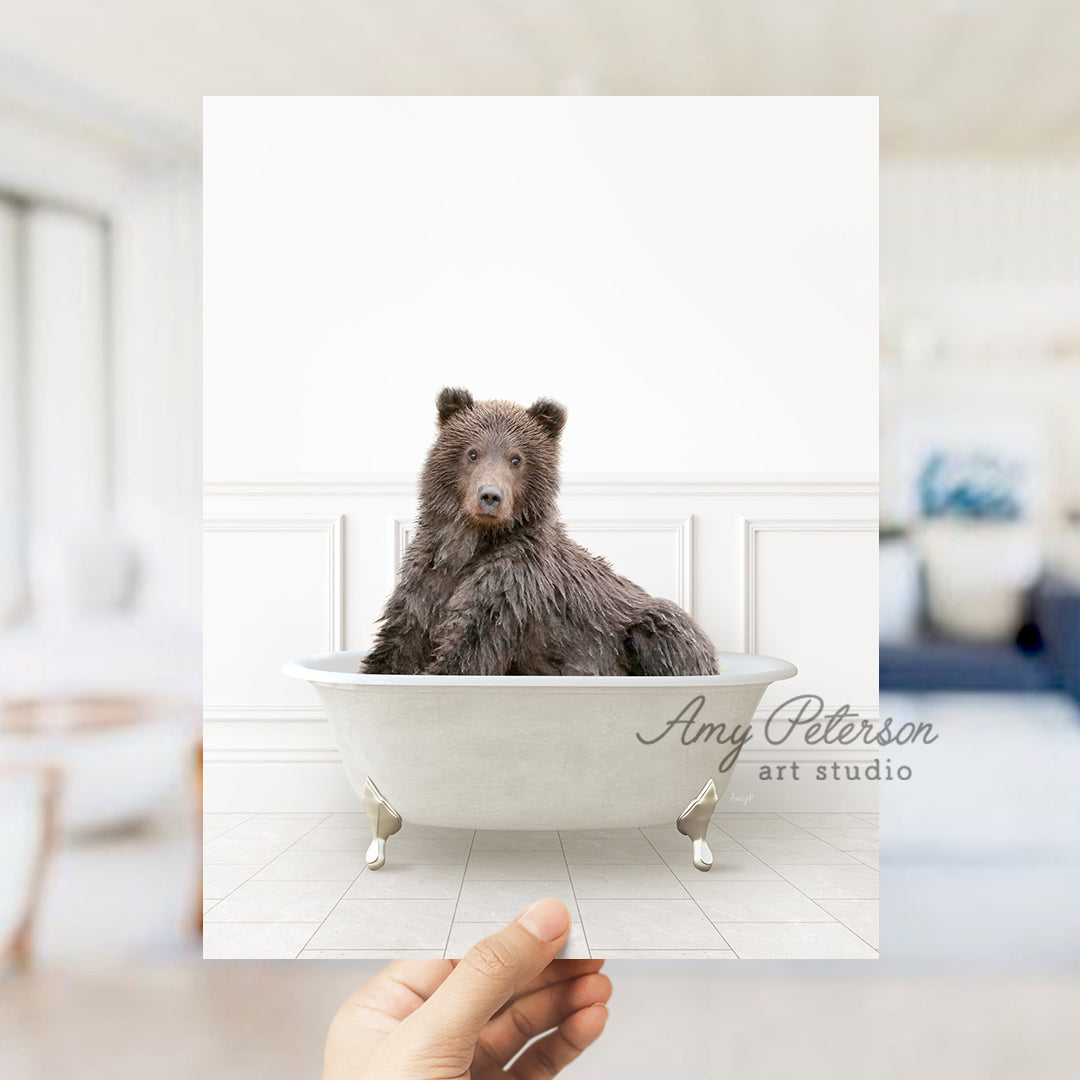 a hand holding up a polaroid picture of a bear in a bathtub