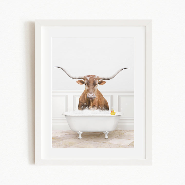 A brown cow with long horns is sitting in a white bathtub filled with water, with a yellow rubber duck floating in the water.