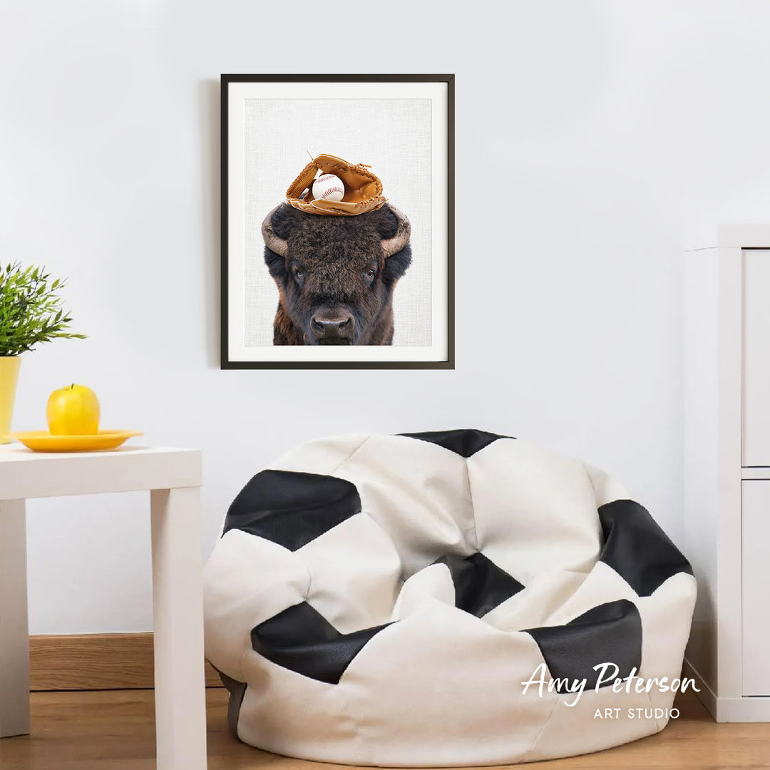 a framed picture of a buffalo with a baseball cap on its head, hanging on a white wall above a black and white bean bag chair.