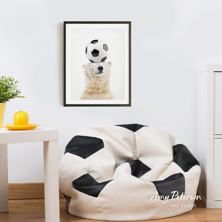 a polar bear balancing a soccer ball on its head, with a framed picture of the polar bear hanging on the wall above a white bean bag chair.