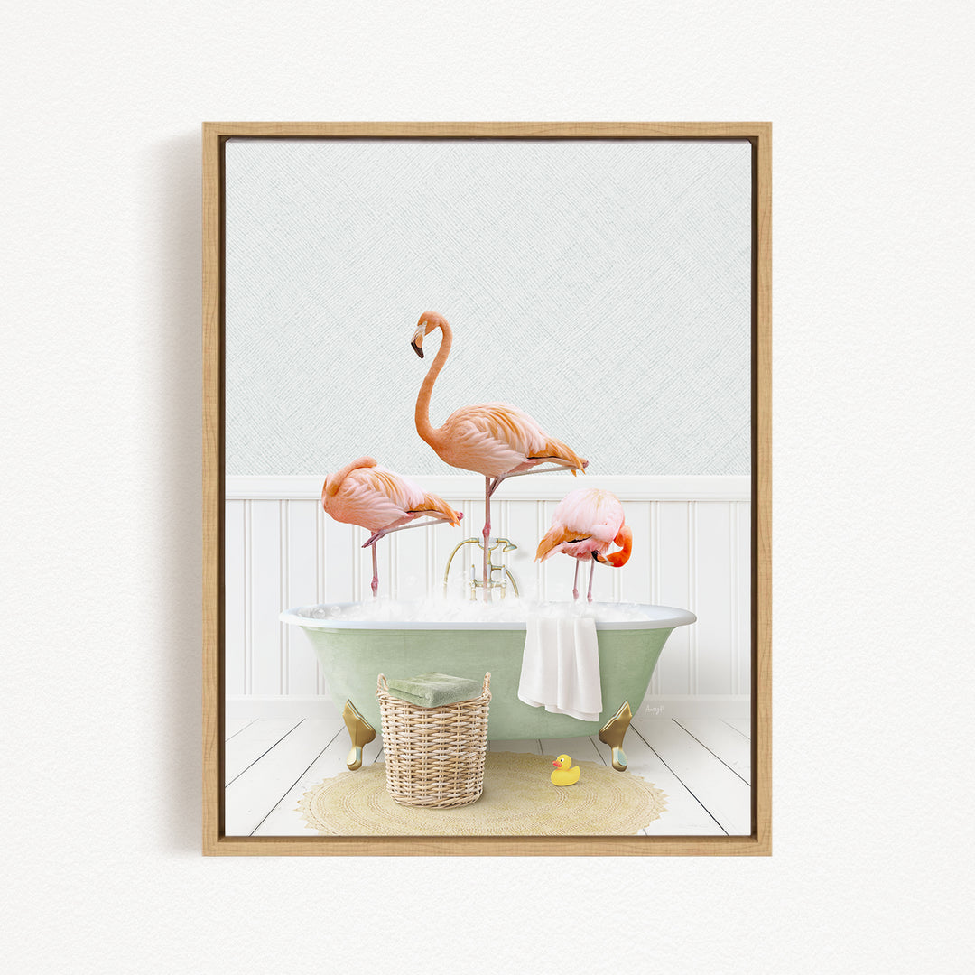 A framed image depicting three pink flamingos standing in a green bathtub filled with water, surrounded by a basket of bath toys and a towel.