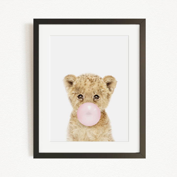 A cute baby lion blowing a bubble with a pink bubble gum bubble.