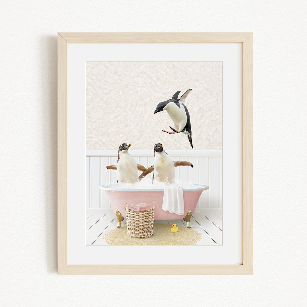 A framed image depicting two penguins sitting in a pink bathtub, with one penguin standing on the edge of the tub and another penguin sitting inside the tub.