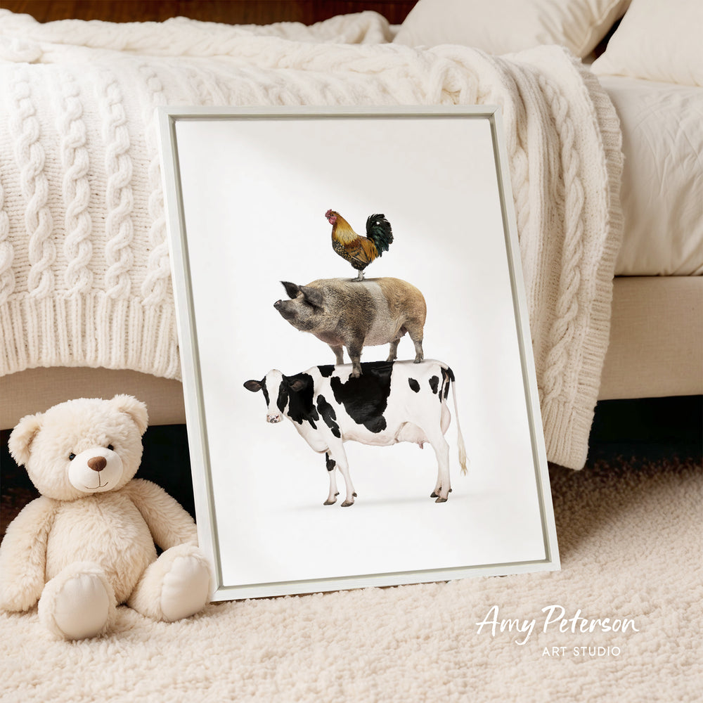 A framed illustration of a pig, cow, and rooster is displayed on a white background, accompanied by a teddy bear and a blanket.