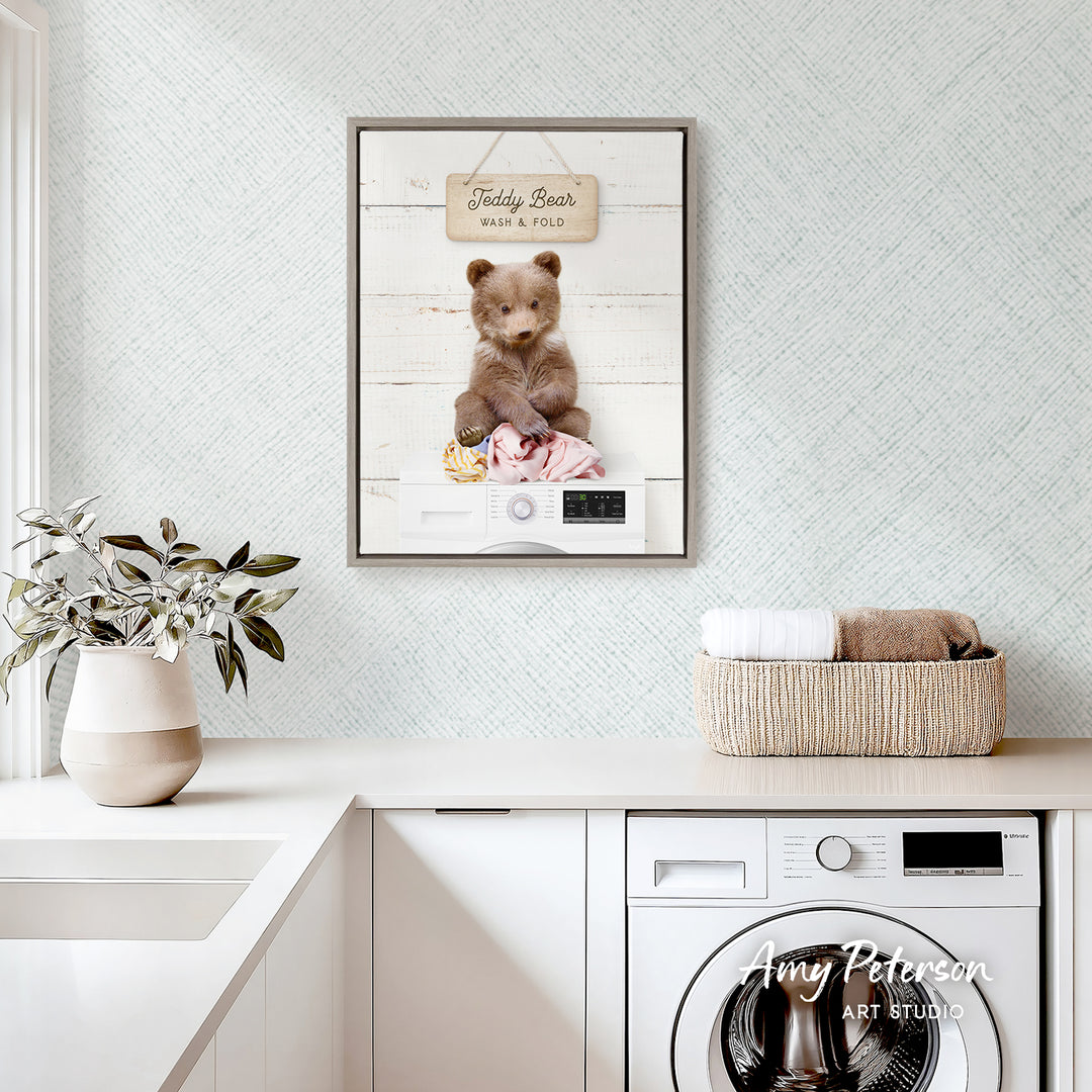 a framed photo of a teddy bear sitting in a basket, placed on a white countertop in a room with a washing machine and a plant.