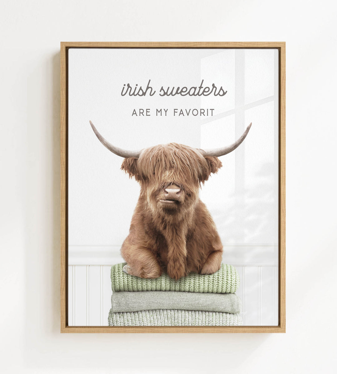 a brown cow with long horns sitting on a stack of green and white sweaters.