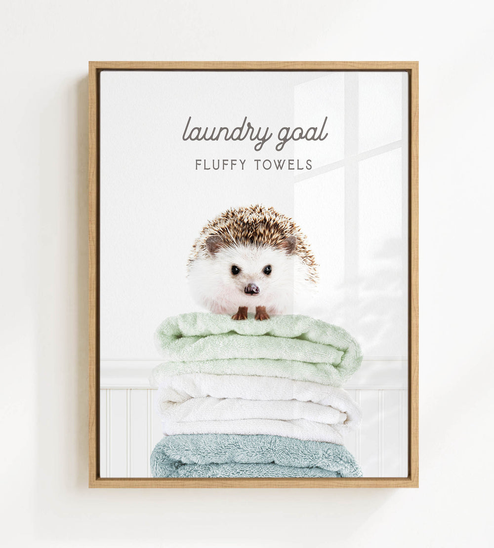 A framed image of a hedgehog sitting atop a stack of fluffy towels, with the text "laundry goal" and "FLUFFY TOWELS" written above it.