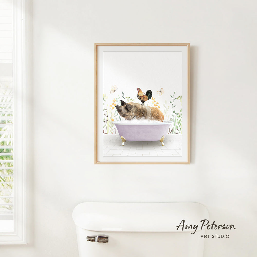 A framed illustration of a pig sitting in a bathtub, surrounded by flowers and a rooster, is hanging on a white wall.