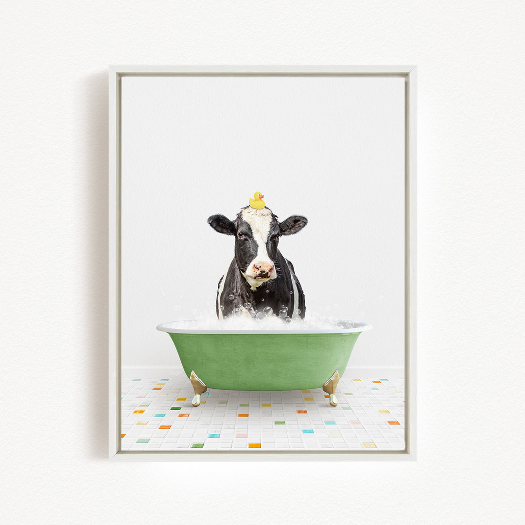 A black and white cow is sitting in a green bathtub filled with bubbles, with a yellow rubber duck perched on its head.