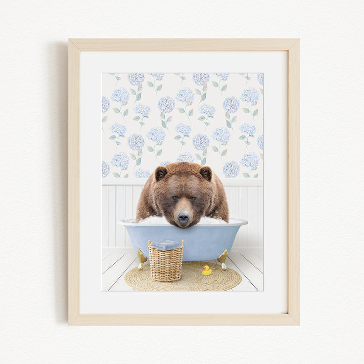 A brown bear is sitting in a blue bathtub filled with water, surrounded by a floral patterned wall and a basket of rubber ducks.