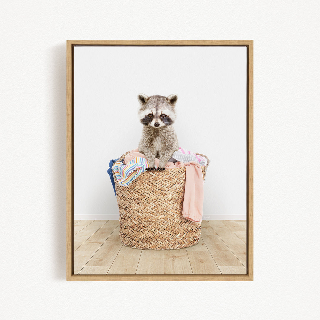 A raccoon sitting in a woven basket filled with clothes.