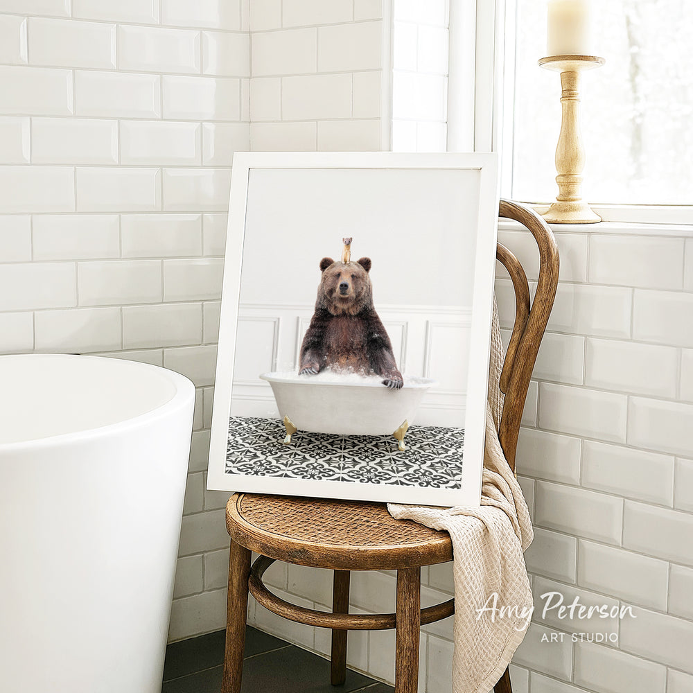 A framed image of a bear sitting in a bathtub, with a crown on its head, is displayed on a wooden chair in a bathroom setting.