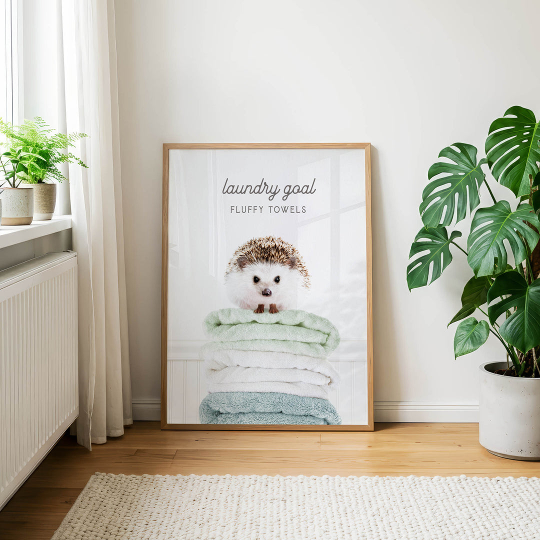 A framed poster of a hedgehog sitting atop a stack of fluffy towels, with the text "laundry goal" and "FLUFFY TOWELS" displayed on the poster.