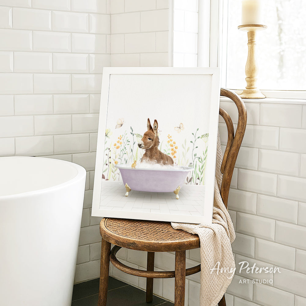 A framed illustration of a dog sitting in a bathtub, surrounded by flowers, is displayed on a wooden chair in a bathroom setting.
