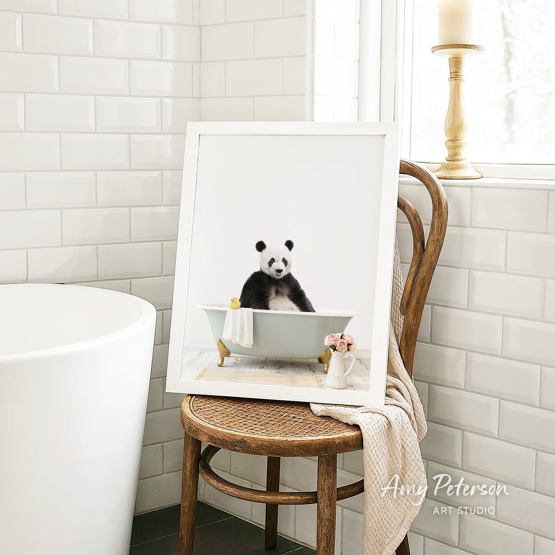 A framed image of a panda sitting in a bathtub, with a vase of flowers and a towel nearby, is displayed on a wooden chair in a bathroom setting.