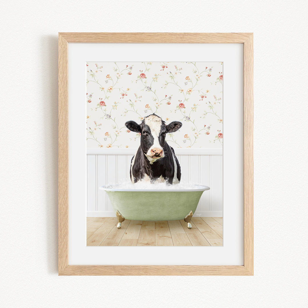 A black and white cow is sitting in a green bathtub filled with bubbles, with a floral wallpaper in the background.