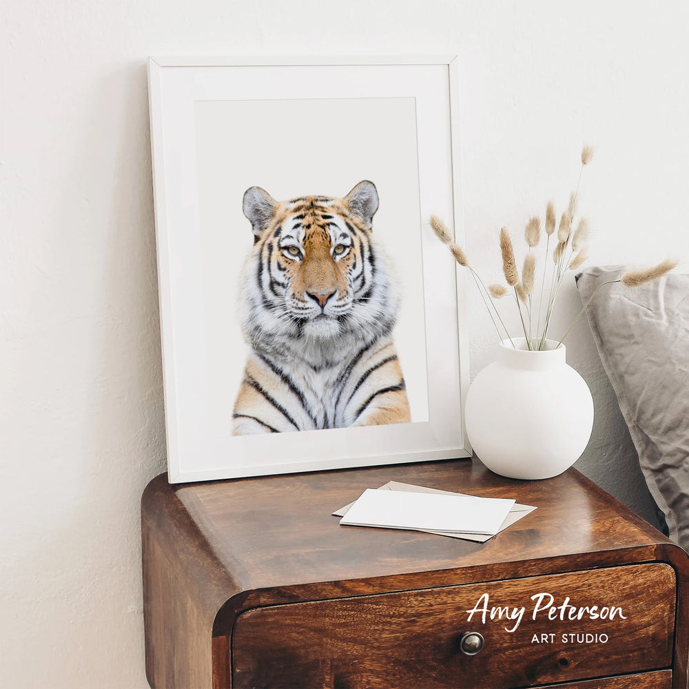 a framed photograph of a tiger on a wooden dresser, with a white vase of dried flowers and a note on the dresser.