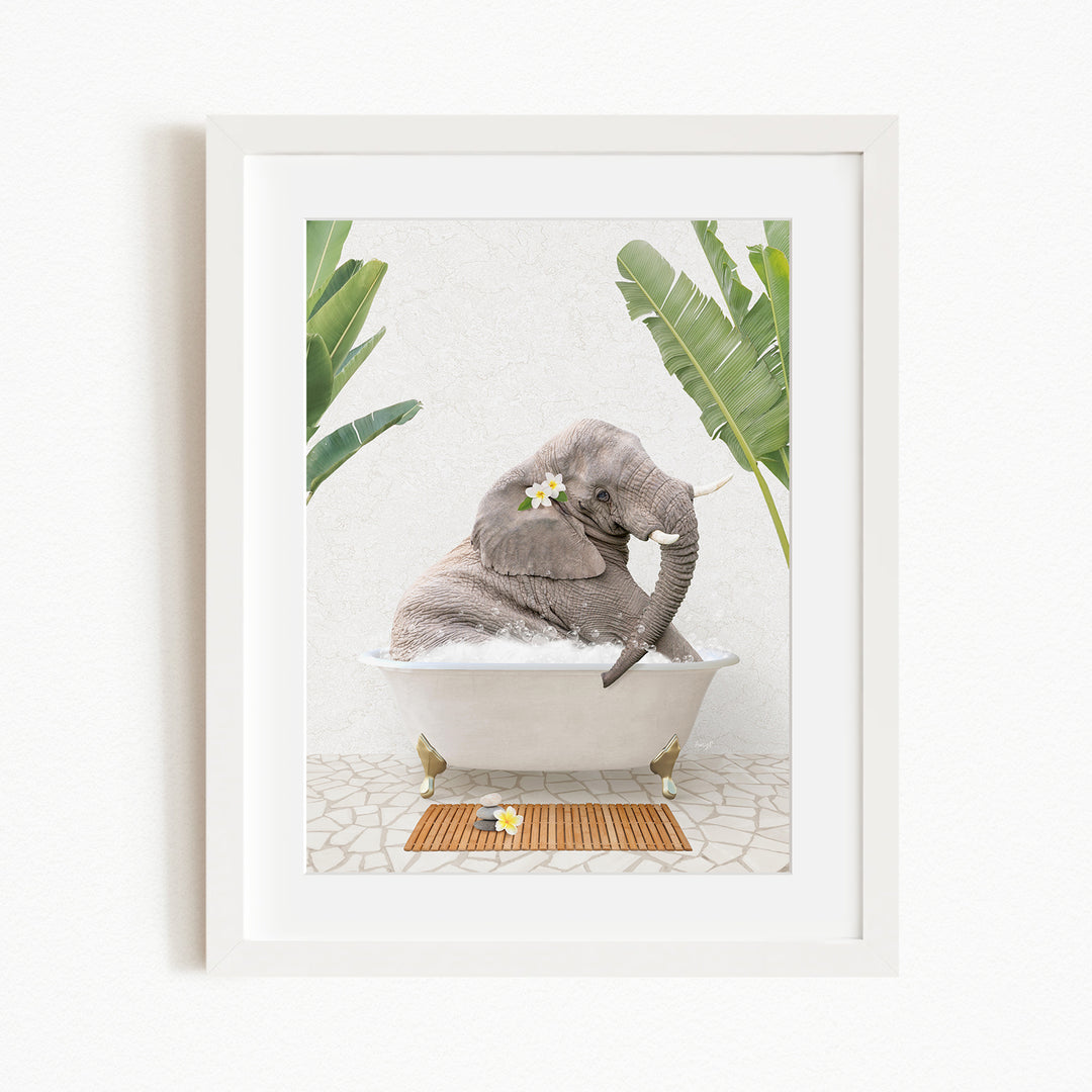 A gray elephant is sitting in a white bathtub, surrounded by green leaves and a wooden mat on the floor.