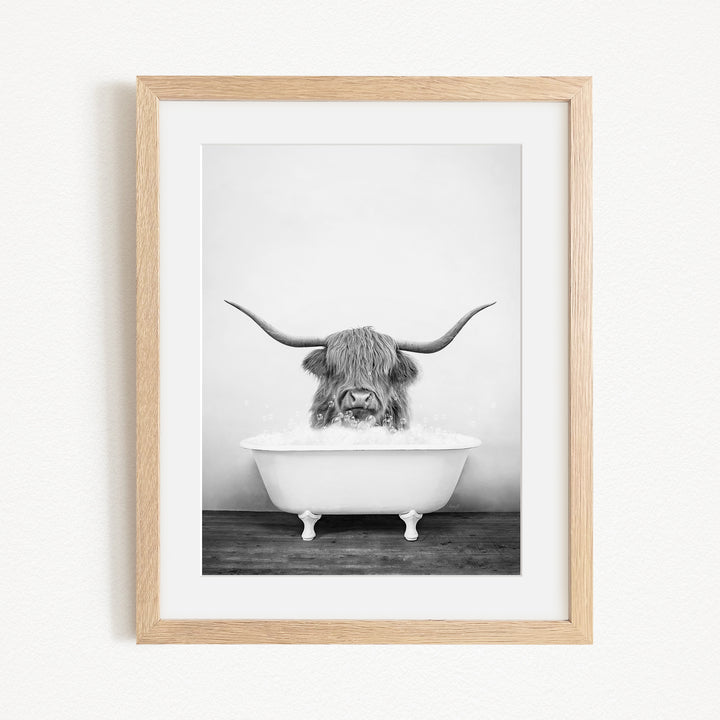 A black and white photograph of a Highland cow with long horns sitting in a bathtub.