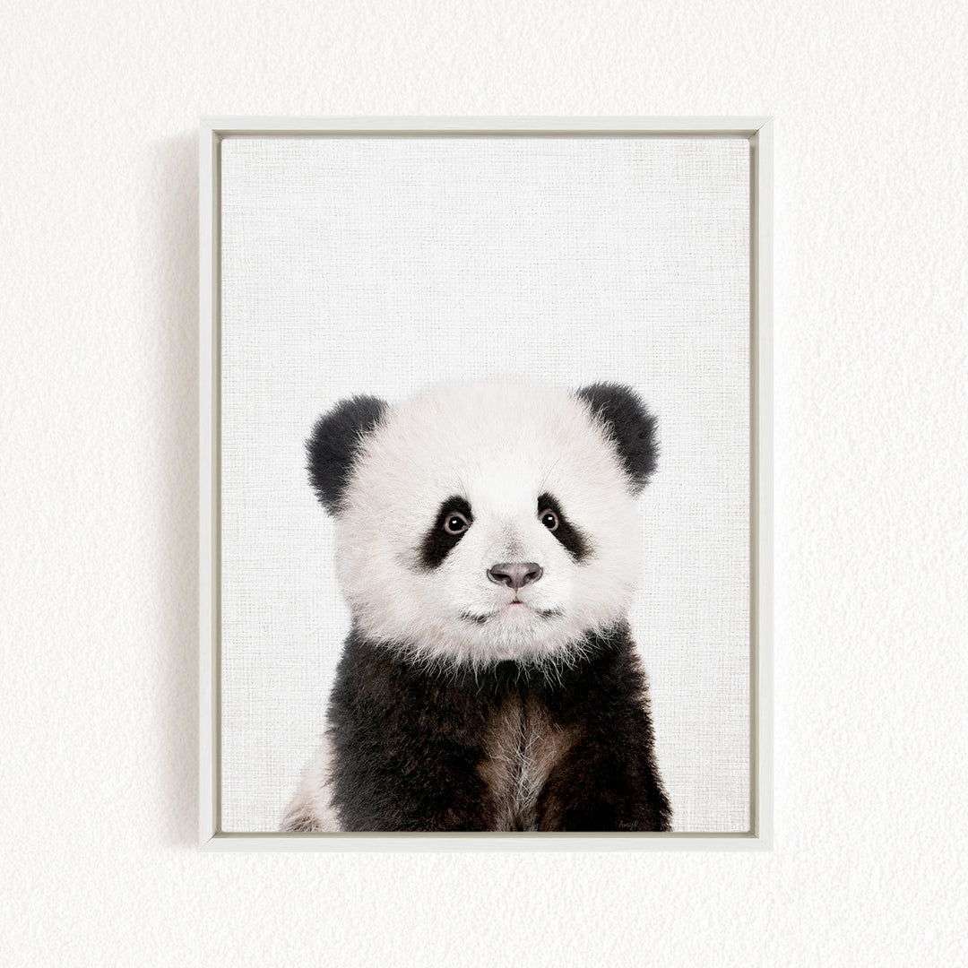 A panda bear with black and white fur is the main subject of the framed print, which is displayed on a white wall.