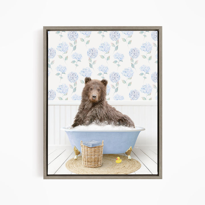 A brown bear sitting in a blue bathtub filled with bubbles, surrounded by a wicker basket and yellow rubber ducks.