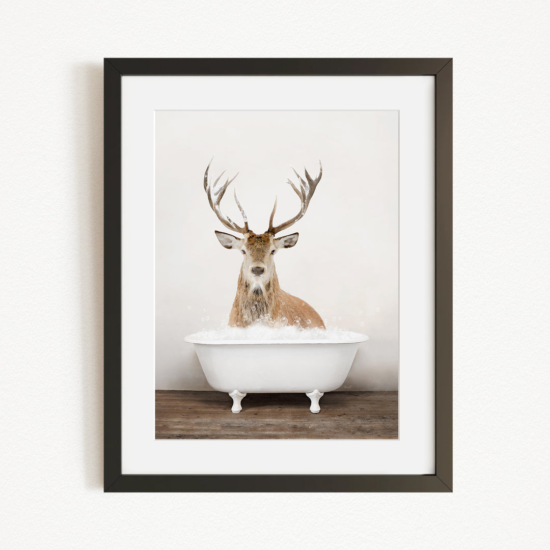 A deer with large antlers is sitting in a white bathtub, surrounded by bubbles.