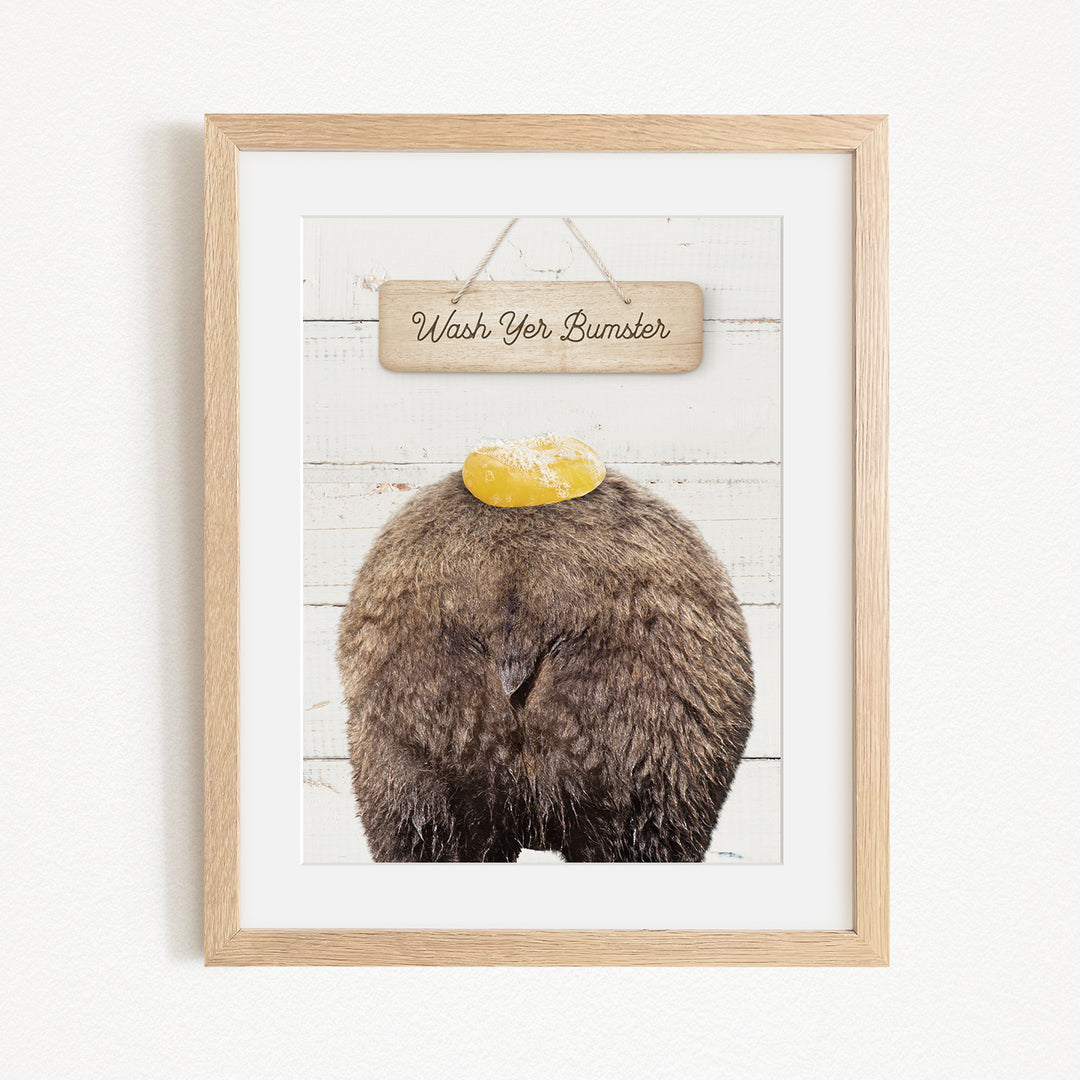 A framed image of a bear with a yellow object on its head, accompanied by a wooden sign that says "Wash Your Bummer".
