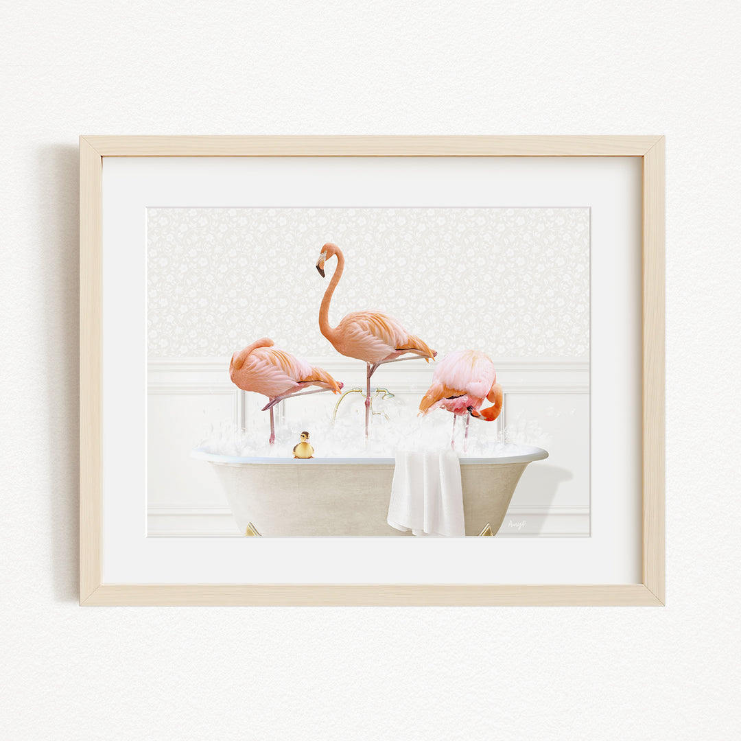 A framed image depicting three pink flamingos standing in a white bathtub filled with water, with a towel draped over the side.