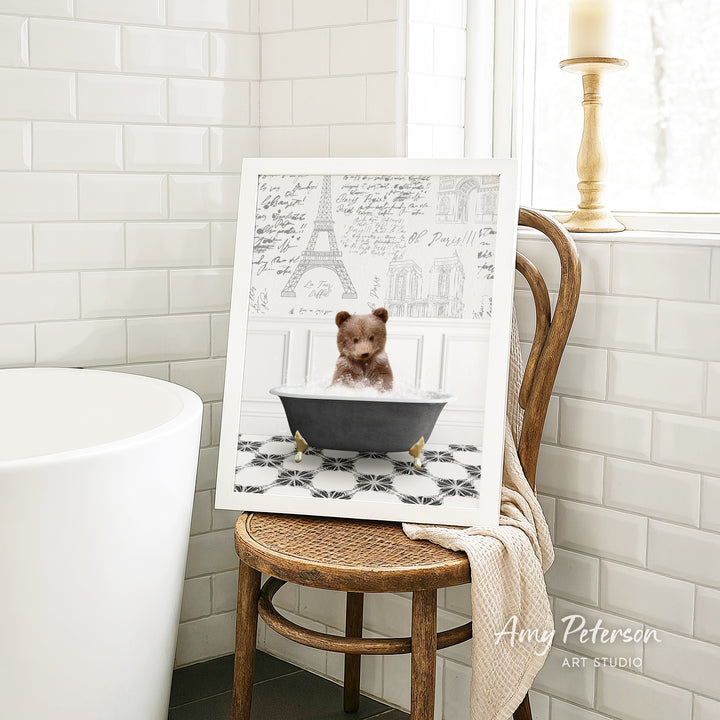 A framed image of a teddy bear sitting in a bathtub, surrounded by a tiled pattern, is displayed on a wooden chair in a bathroom setting.