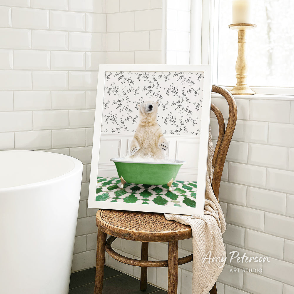 A framed image of a polar bear sitting in a green bathtub, surrounded by a patterned design, is displayed on a wooden chair in a bathroom setting.