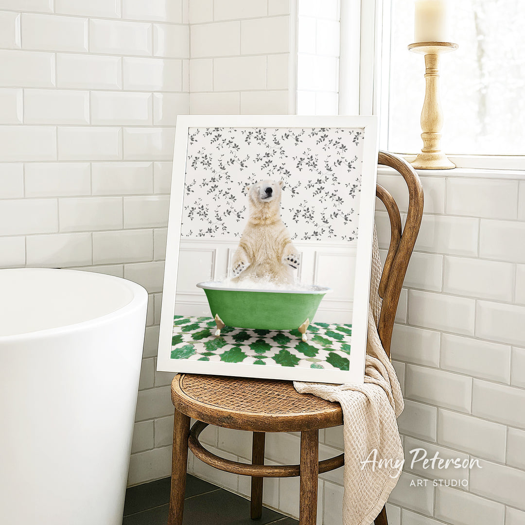 A framed image of a polar bear sitting in a green bathtub, surrounded by a patterned design, is displayed on a wooden chair in a bathroom setting.