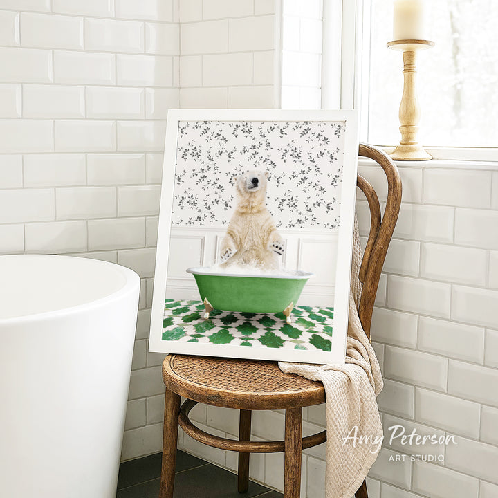 A framed image of a polar bear sitting in a green bathtub, surrounded by a patterned design, is displayed on a wooden chair in a bathroom setting.