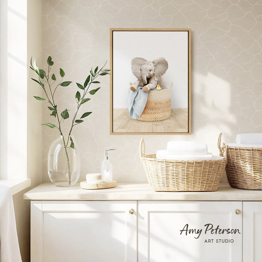 a framed photograph of an elephant sitting in a basket, placed on a wall above a white cabinet with two woven baskets.