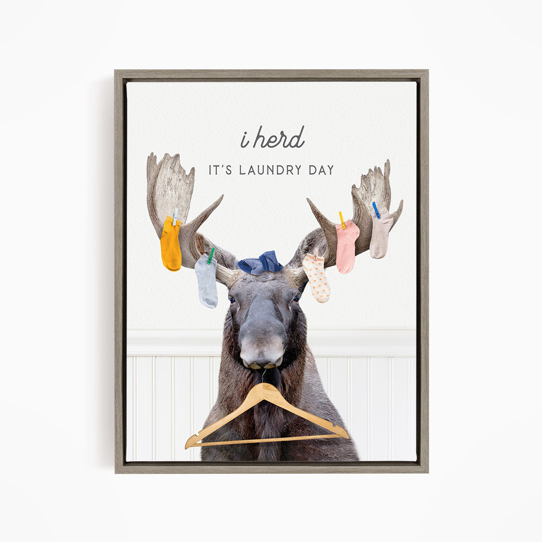 A framed print featuring a cartoon image of a moose with a laundry basket, displaying socks hanging from its antlers.