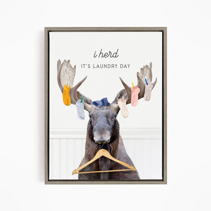 A framed print featuring a cartoon image of a moose with a laundry basket, displaying socks hanging from its antlers.