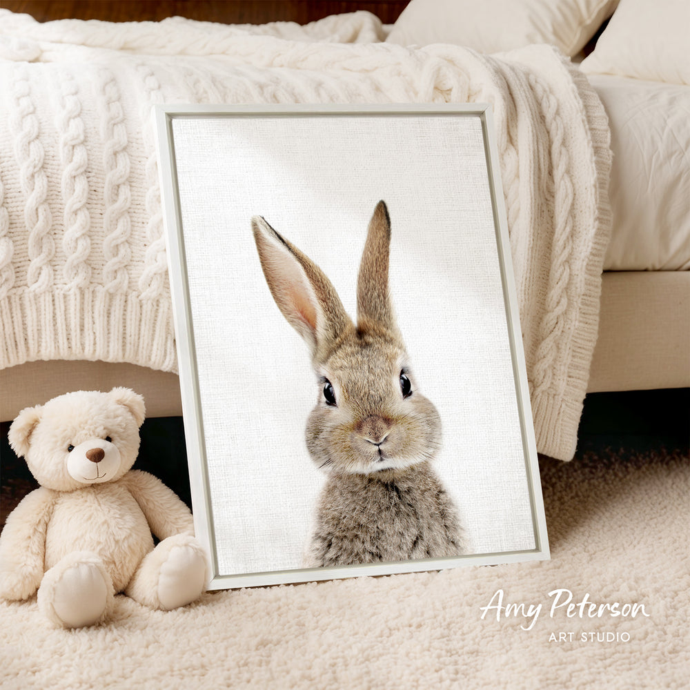 A framed image of a rabbit is displayed on a bed, accompanied by a teddy bear.